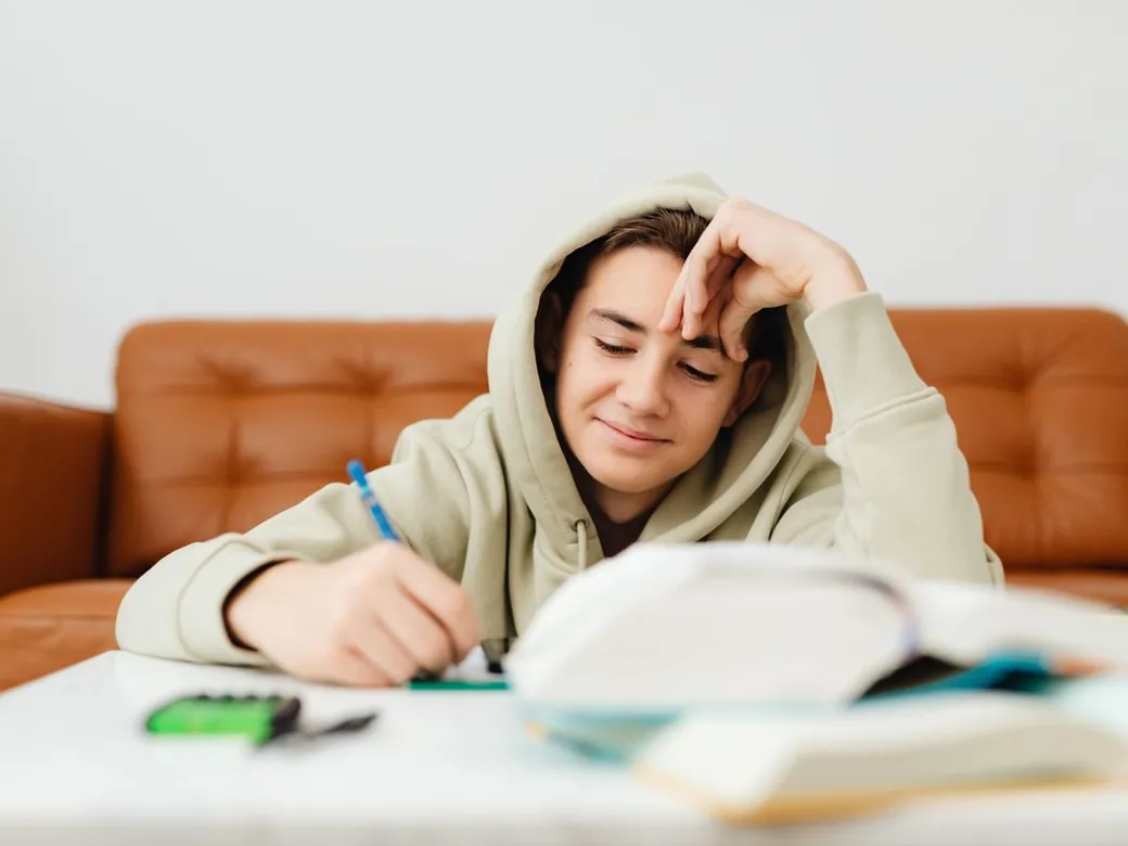 A secondary school pupil making notes with a calculator and textbooks.
